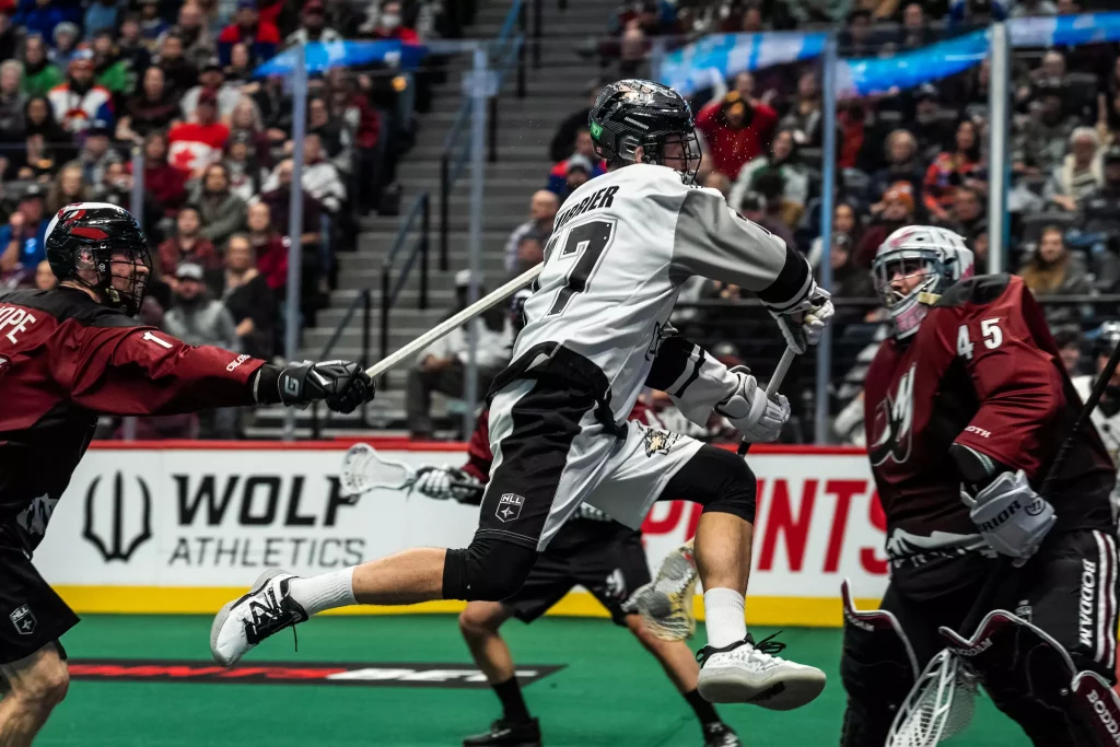 a lacrosse player reaches for the ball, with an opponent in the background