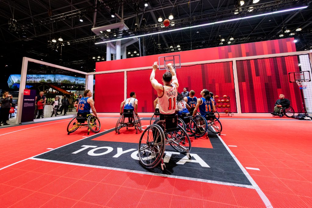 a wheelchair basketball player reaches to shoot a basket, they play on a toyota-branded court