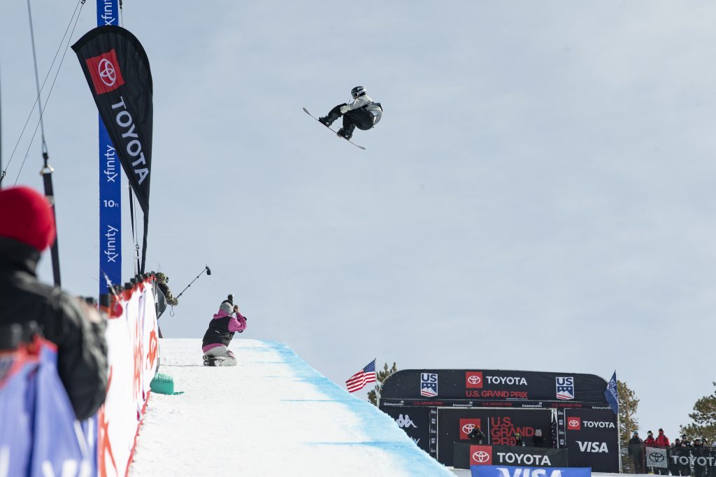 a snowboarder performs a grab on the edge of a halfpipe in competition 